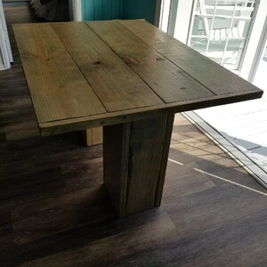 May include: A rustic wooden table with a natural wood finish. The table has a rectangular top and a single pedestal base. The table is made of reclaimed wood and has a distressed look.