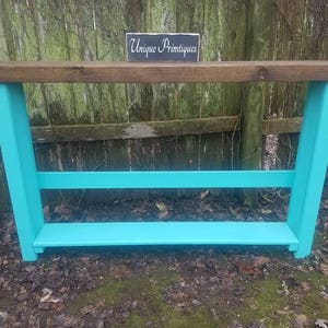 May include: A turquoise console table with a wooden top. The table has a shelf and is made of wood. The table is in front of a wooden fence.