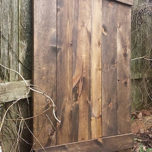 May include: A dark brown wooden door with a horizontal plank across the middle. The door is made of vertical planks and has a rustic look.