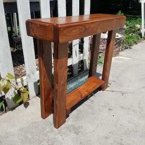 May include: A rustic wooden console table with a dark brown stain. The table has a single shelf and a sign that reads "Unique Printables".