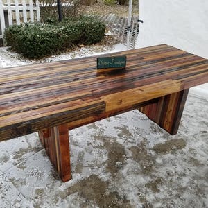 May include: A rustic wooden table with a reclaimed wood top and legs. The table is made of various shades of brown wood and has a natural, distressed finish. The table is sitting on a snowy surface. A small sign on the table reads "Unique Antiques".