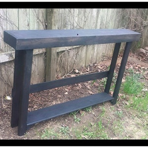 May include: A black wooden console table with a single shelf. The table has a rustic, farmhouse style and is made of reclaimed wood.