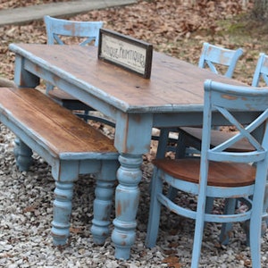 May include: A rustic dining set with a distressed blue finish. The set includes a rectangular table, a bench, and three chairs. The table has a brown wooden top and a sign that reads "UNIQUE PRIMTIQUES".