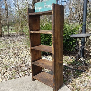 May include: A rustic wooden shelf unit with four shelves. The shelf unit is stained a dark brown color and has a sign on top that reads "Unique Primitive".