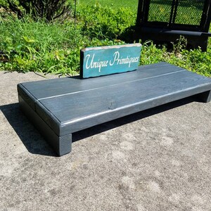 May include: A dark gray wooden platform with a teal sign that reads "Unique Primitives".