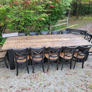 May include: A large rectangular wooden dining table with a dark brown stained top and black legs, surrounded by ten black wooden chairs with cross-back designs and brown seats. Two small rectangular signs are placed on the table surface.