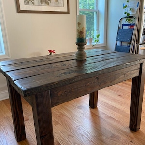 May include: A dark brown wooden table with a rustic finish. The table has a rectangular top and four legs. The table is made of reclaimed wood and has a natural wood grain.