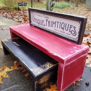 May include: A red and black wooden step stool with a sign that reads "Rustic Farmhouse Furniture Unique Primitives & Decor" on top.