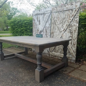 May include: A rustic farmhouse style dining table with a distressed gray wood top and dark stained legs. The table has a simple, rectangular shape with turned legs and a stretcher.