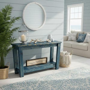 May include: A rectangular blue wooden console table with a lower shelf, featuring a distressed finish. On the shelf sits a rectangular sign with the text Unique Primtiques. The table is topped with a glass lantern containing a white candle.