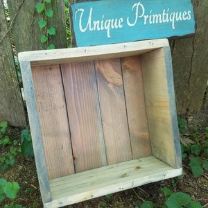 May include: A rustic wooden box with a distressed gray and brown finish. The box is empty and has a sign above it that reads "Unique Primitives".