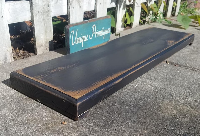 May include: A black wooden shelf with a distressed finish. The shelf is sitting on a concrete surface. A sign that reads "Unique Primtiques" is in the background.