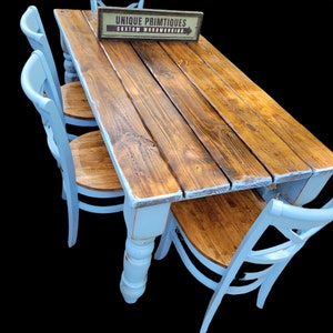 May include: A rustic wooden dining table with four matching chairs. The table has a distressed brown tabletop and white-painted legs. The chairs are light blue with wooden seats. A sign above the table reads "UNIQUE PRIMTIQUES CUSTOM WOODWORKING".