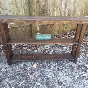 May include: A dark brown wooden console table with two shelves. The table has a rustic, farmhouse style. The top shelf has a small sign that reads "Unique Printables".