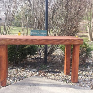 May include: A rustic wooden table with a dark reddish-brown stain. The table has a rectangular top and four legs. A small wooden sign with the text "Unique Finds Boutique" is on the table.