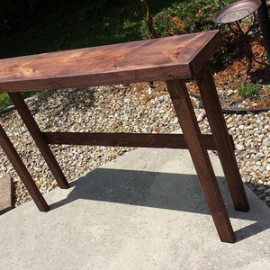 K&ouml;nnte beinhalten: Ein dunkelbrauner Holz-Konsolentisch mit schlichtem Design. Der Tisch hat eine rechteckige Tischplatte und vier Beine. Der Tisch ist aus massivem Holz gefertigt und hat eine nat&uuml;rliche Oberfl&auml;che.