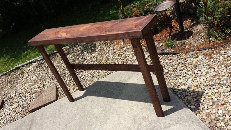 K&ouml;nnte beinhalten: Ein dunkelbrauner Holz-Konsolentisch mit schlichtem Design. Der Tisch hat eine rechteckige Tischplatte und vier Beine. Der Tisch ist aus massivem Holz gefertigt und hat eine nat&uuml;rliche Oberfl&auml;che.