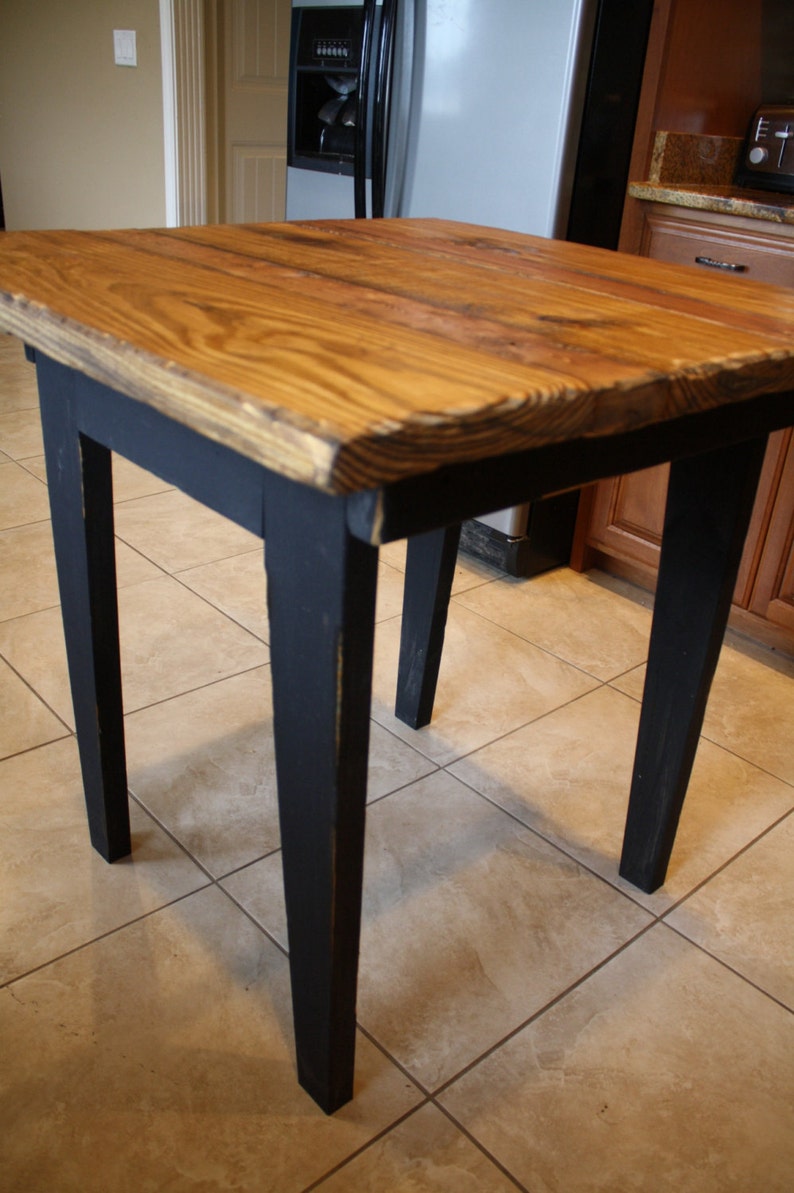 Puede incluir: Una mesa de madera r&uacute;stica con una tapa de madera natural y patas pintadas de negro. La mesa tiene un dise&ntilde;o de borde vivo y es perfecta para una cocina de estilo r&uacute;stico o industrial.