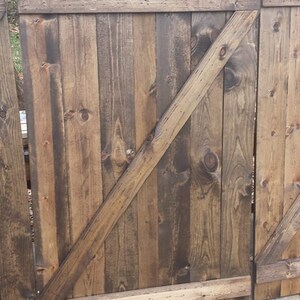 May include: A wooden gate with a diagonal brace, stained in a dark brown color. The gate is made of vertical planks and has a horizontal top rail.