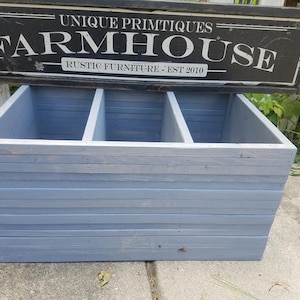 May include: A light blue wooden storage box with three compartments. The box is made of reclaimed wood and has a rustic farmhouse style. The box is labeled "UNIQUE PRIMITQUES FARMHOUSE RUSTIC FURNITURE - EST 2010".