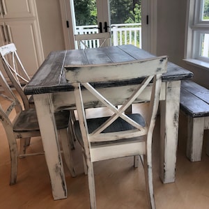 May include: A white farmhouse style dining table with a distressed wood top and matching chairs. The table has a bench on one side.