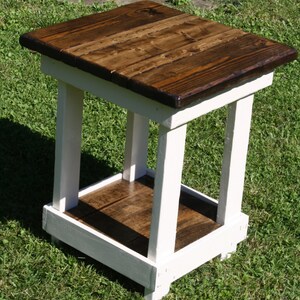 May include: A white wooden end table with a dark brown stained top and shelf. The table has a simple, farmhouse style.