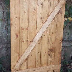 May include: A wooden door with a diagonal brace. The door is made of light brown wood planks and has a natural wood finish.