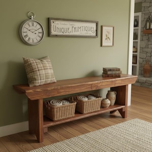 May include: A long wooden bench with a lower shelf holding two woven wicker baskets and a ceramic pitcher. A plaid throw pillow sits on the bench seat. Above the bench, a round wall clock and a rectangular sign reading UNIQUE PRIMTIQUES.