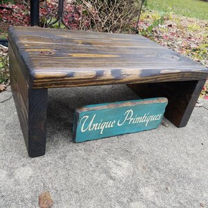 May include: A dark stained wooden stand with a unique design. The stand is made of reclaimed wood and has a rustic look. It is perfect for displaying small items or plants. The stand is labeled "Unique Primtiques".