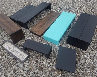 May include: A collection of eight wooden steps or risers in various sizes and colors. The steps are painted black, brown, and turquoise. The steps are arranged on a gravel surface. A sign with the text "Unique Primitiques" is in the lower left corner of the image.