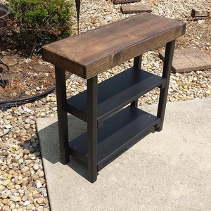 May include: A wooden table with a dark brown top and black metal legs. The table has two shelves for storage.