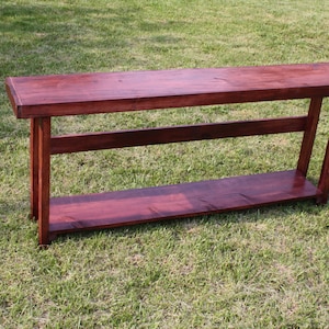 May include: A dark wood console table with a single shelf. The table has a rich, reddish-brown stain and a simple, rectangular design.