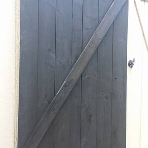 May include: A black wooden barn door with a diagonal brace and two horizontal planks. The door is closed and appears to be made of reclaimed wood.