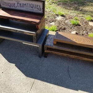 May include: Two sets of tiered wooden risers with a dark stained finish. The left set features a sign with the text UNIQUE PRIMTIQUES & decor. Each set consists of two rectangular platforms stacked to create varying heights for display purposes.