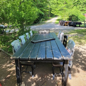 May include: A black farmhouse table with a distressed finish and eight chairs. The table is set up outdoors with a sign that reads "Gather Together".