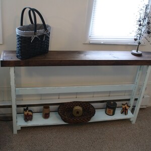 May include: A light blue console table with a dark brown wooden top. The table has two shelves and is decorated with a woven basket, a small tin can, and a wooden star.