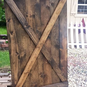 May include: A rustic wooden door with a dark brown stain and a diagonal X-shaped design. The door is made of vertical planks and has a dark brown stain.