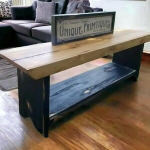 May include: A rustic wooden bench with a black painted base and a natural wood top. The bench has a shelf underneath and is decorated with a sign that reads "Unique Primitives".