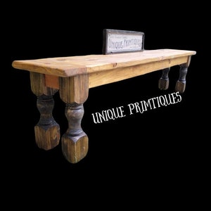 May include: A rustic wooden shelf with turned legs. The shelf is stained a dark brown color and has a natural wood finish. The shelf is labeled "UNIQUE PRIMITQUES".