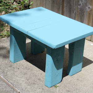 May include: A light blue wooden table with a simple design. The table has four legs and a rectangular top. The table is made of solid wood and has a smooth finish.