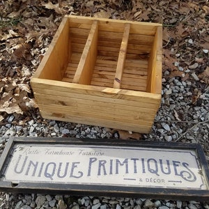 May include: A wooden box with three compartments, made of natural wood with a rustic finish. The box is sitting on a bed of gravel and leaves. A sign with the text "Rustic Farmhouse Furniture Unique Primitives & Décor" is in the foreground.