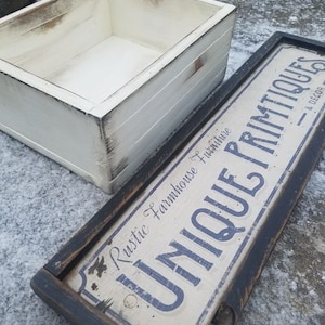 May include: A white wooden box with a distressed finish and a black wooden frame with a sign that reads "Unique Primitives Rustic Farmhouse Furniture & Decor".