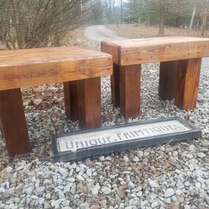 May include: Two rustic wooden stools with a natural wood finish. The stools are made of reclaimed wood and have a simple, farmhouse style. The stools are sitting on a gravel surface with a sign that reads "Unique Primitives" in front of them.