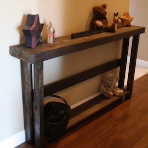May include: A dark brown wooden console table with a shelf. The table has a rustic look and is decorated with a star, a teddy bear, and a sign that reads "For Every Season, Always Remember What Matters".