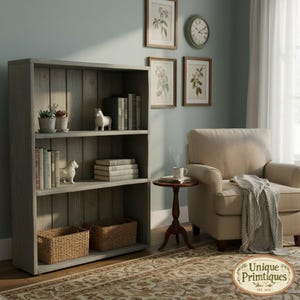 May include: A tall, gray wooden bookcase with three shelves, featuring vertical plank backing. The shelves hold potted plants, books, two small horse figurines, and two woven baskets. Beside the bookcase sits a beige armchair and a small round table.