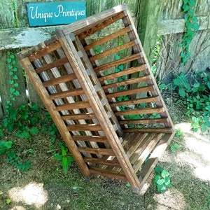 May include: A wooden crate with a slatted design, stained in a dark brown color. The crate is sitting on a bed of green grass and wood chips. A sign with the text "Unique Primtiques" is visible in the background.