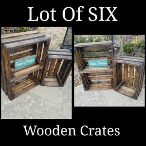 May include: Lot of six wooden crates, stained dark brown with black accents. The crates are stacked in two different configurations. One configuration has two crates stacked on top of each other, and the other configuration has three crates stacked on top of each other. The crates have a shelf in the middle. The crates have a sign that says "Unique Printiques" on the shelf.