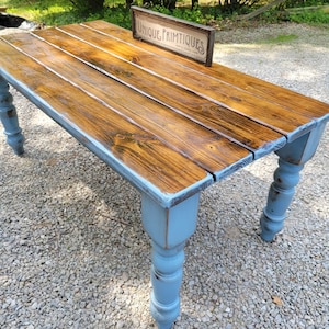 May include: A rustic wooden table with a stained brown tabletop and distressed blue legs. The table features a sign that reads "UNIQUE PRIMTIQUES". The table is made of wood and is suitable for indoor or outdoor use.