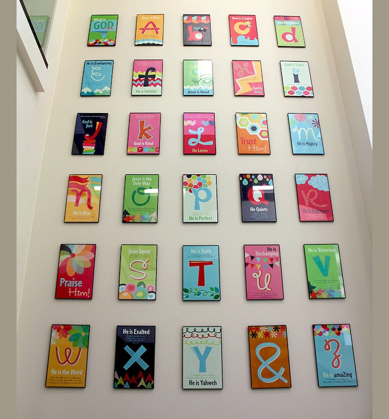 K&ouml;nnte beinhalten: Eine Wandanzeige mit bunten gerahmten Postern mit Buchstaben des Alphabets und religi&ouml;sen S&auml;tzen. Jedes Poster hat ein anderes Farbschema und Design, mit einem Buchstaben und einem Satz, der sich auf Gott oder Jesus bezieht. Die S&auml;tze beinhalten "Gott ist gerecht", "Er ist ewig", "Jesus ist gut", "Er ist nah", "Gott ist g&uuml;tig", "Er liebt", "Vertraue ihm", "Er ist m&auml;chtig", "Jesus ist der einzige Weg", "Er ist perfekt", "Er beruhigt", "Er ist siegreich", "Lobt ihn", "Jesus rettet", "Er ist das Wort", "Er ist erh&ouml;ht", "Er ist Jahwe", "Er ist erstaunlich".