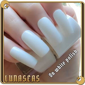 Puede incluir: U&ntilde;as largas de forma cuadrada pintadas con un esmalte de u&ntilde;as blanco s&oacute;lido y opaco. El texto "LUNASEAS" aparece en la esquina inferior izquierda y el texto "On white polish" est&aacute; impreso en la zona inferior derecha.